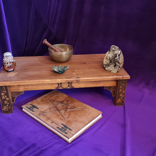 May include: A wooden altar table with a book, a singing bowl, a crystal, and a bottle of liquid on top. The table has intricate carvings on the legs and a pentagram design on the book.