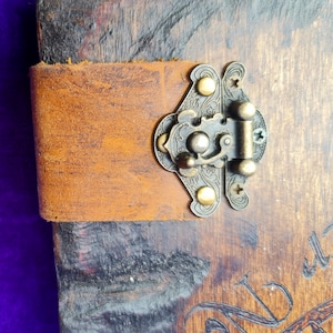 以下が含まれることがあります： 真鍮の留め金と装飾的なアクセントが付いた、茶色の革装丁のジャーナル。ジャーナルは使い古したヴィンテージな外観で、閉じられています。