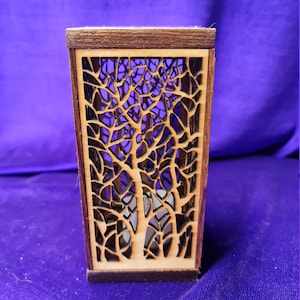 Könnte beinhalten: Ein Kerzenhalter aus Holz mit einem Laser-geschnittenen Design von zwei Bäumen. Der Halter ist aus hellbraunem Holz mit dunkelbraunem Rand.