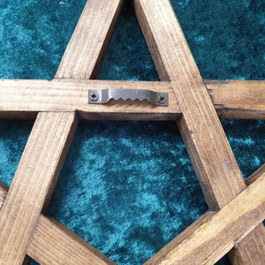 May include: A wooden five-pointed star with a metal hanging loop on the back. The star is stained a dark brown color and has a rustic appearance.