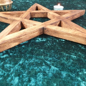 May include: A wooden pentagram with a dark brown stain, lying on a green velvet surface. The pentagram is a five-pointed star with a hollow center.