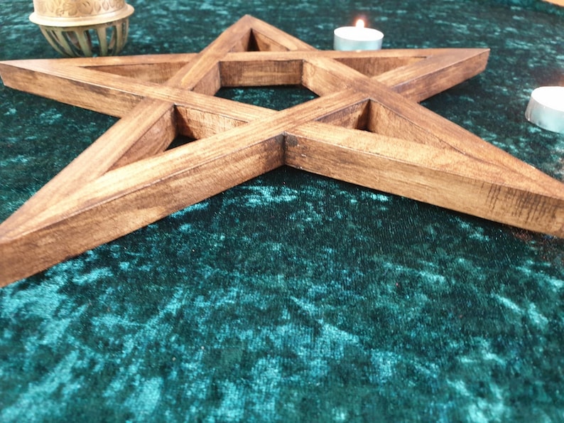 May include: A wooden pentagram with a dark brown stain, lying on a green velvet surface. The pentagram is a five-pointed star with a hollow center.