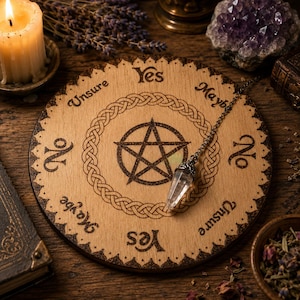 May include: A circular wooden dowsing board featuring a central pentagram, a decorative braided border, and the words Yes, No, Maybe, and Unsure printed around the edge. A clear crystal pendulum on a metal chain rests on the board surface.