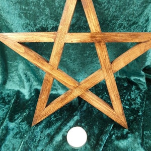 May include: A wooden five-pointed star, also known as a pentagram, is displayed on a green velvet surface. A white candle sits below the star.