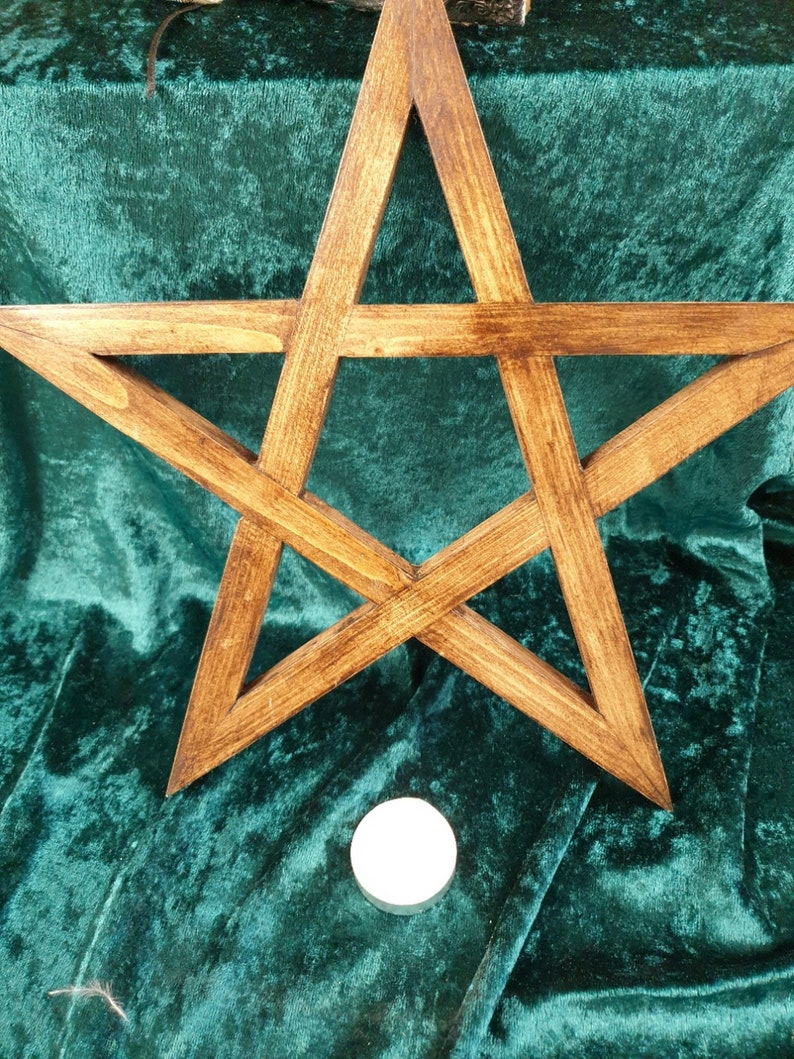 May include: A wooden five-pointed star, also known as a pentagram, is displayed on a green velvet surface. A white candle sits below the star.