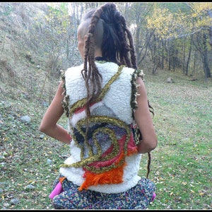 Puede incluir: Un chaleco blanco con detalles de tela coloridos y un diseño en capas. El chaleco lo lleva una persona con rastas largas de color marrón oscuro.