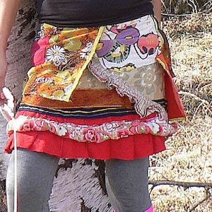 Peut inclure: Une femme portant un débardeur noir, une jupe en patchwork colorée et des chaussettes roses. Elle se tient à côté d'un bouleau.