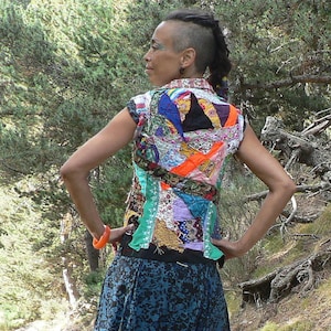 Puede incluir: Una mujer con un chaleco de patchwork colorido, una falda azul oscuro y calcetines rojos y blancos. Está de pie en un entorno boscoso.