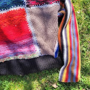 May include: A colourful patchwork knit sweater with a striped sleeve. The sweater is made of different coloured yarns and has a crocheted border.