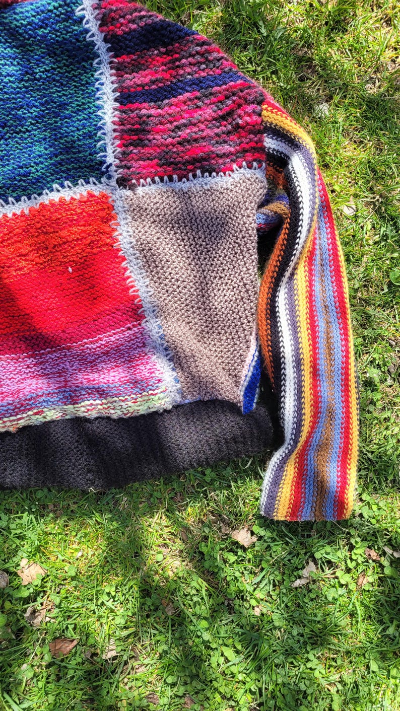 May include: A colourful patchwork knit sweater with a striped sleeve. The sweater is made of different coloured yarns and has a crocheted border.