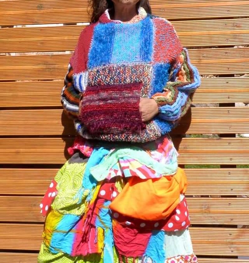 May include: A colourful patchwork sweater with a large pocket on the front. The sweater is made of different coloured yarns and has a fuzzy texture. The sweater is worn over a colourful patchwork skirt.
