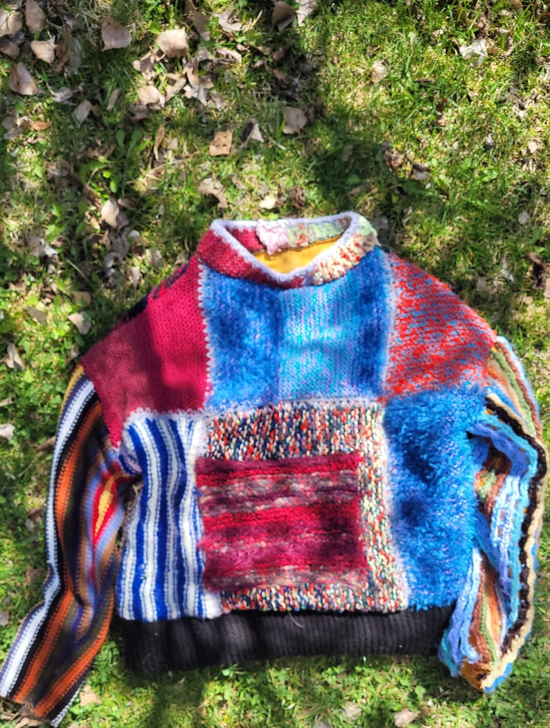 May include: A colourful patchwork sweater with a variety of textures and patterns. The sweater is made of different coloured yarns, including red, blue, white, and black. The sweater has a crew neck and long sleeves.