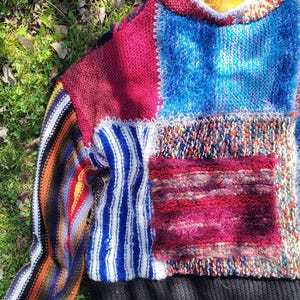 May include: A colourful patchwork sweater with a variety of knit textures and patterns. The sweater has a black ribbed hem and a striped sleeve.