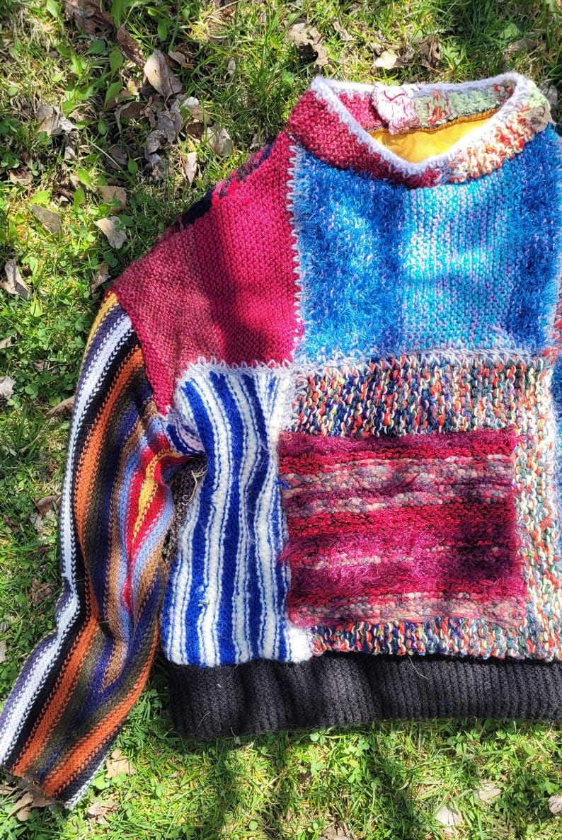 May include: A colourful patchwork sweater with a variety of knit textures and patterns. The sweater has a black ribbed hem and a striped sleeve.