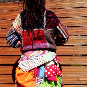 May include: A person wearing a colourful patchwork sweater and a skirt made of various patterned fabrics. The skirt is layered and has a bohemian style.