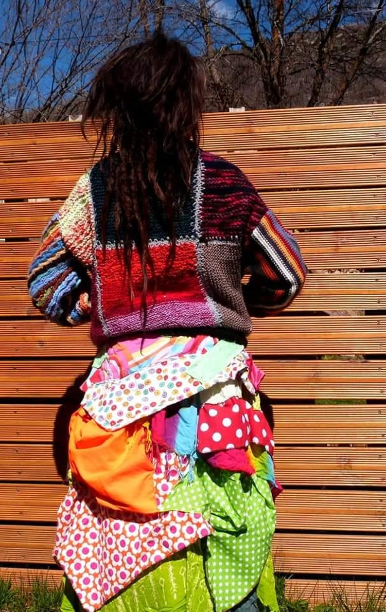 May include: A person wearing a colourful patchwork sweater and a skirt made of various patterned fabrics. The skirt is layered and has a bohemian style.