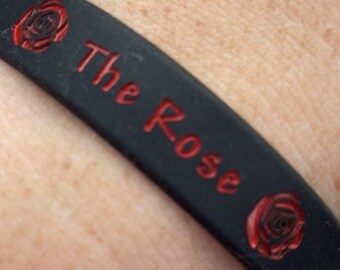 May include: Black silicone wristband with red roses and the text "The Rose" printed on it.
