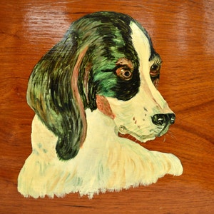 Puede incluir: Una imagen pintada de la cabeza de un perro sobre una superficie de madera. El perro tiene pelo blanco con marcas negras y verdes. Los ojos del perro son marrones y la nariz es negra.