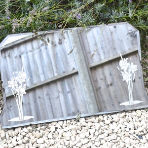 May include: A vintage beveled mirror with a decorative etched design of white flowers. The mirror has a silver frame and is sitting on a bed of white gravel.