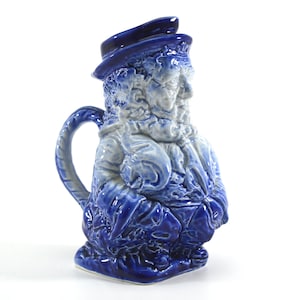 Puede incluir: Una jarra de cerámica azul y blanca con forma de hombre con sombrero y barba. La jarra tiene un asa y un pico.