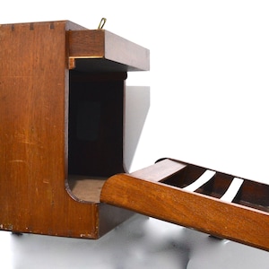 K&ouml;nnte beinhalten: Ein wandmontiertes Aufbewahrungselement aus Holz mit einer ausziehbaren Schublade und einem Regal. Die Schublade hat einen kleinen Messingknopf und das Regal hat einen kleinen Messinggriff.