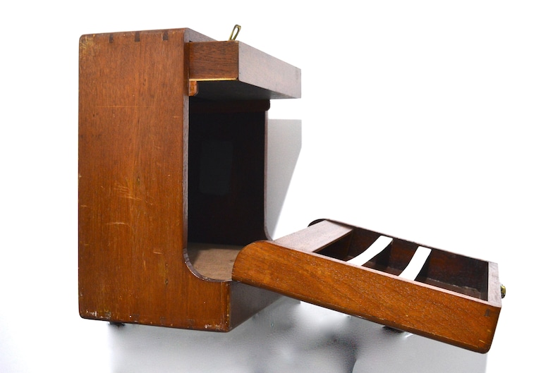 K&ouml;nnte beinhalten: Ein wandmontiertes Aufbewahrungselement aus Holz mit einer ausziehbaren Schublade und einem Regal. Die Schublade hat einen kleinen Messingknopf und das Regal hat einen kleinen Messinggriff.