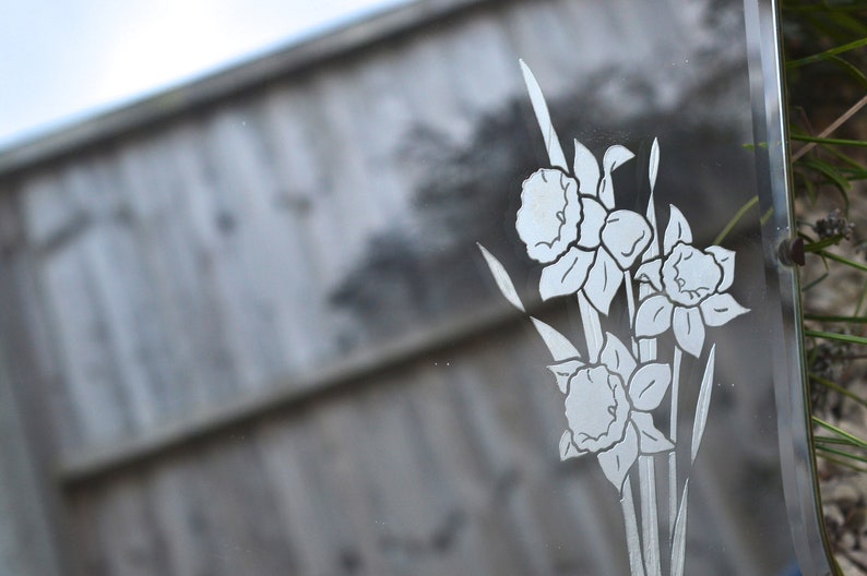 May include: A vintage mirror with an etched design of white flowers on a clear glass surface.