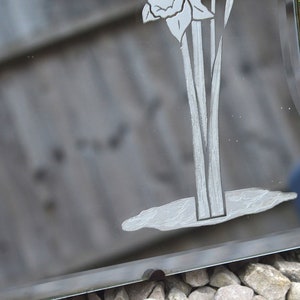 May include: A vintage beveled mirror with an etched design of a flower with long stems. The mirror has a dark gray background and a silver-colored etched design.