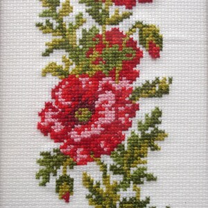 May include: Cross-stitch embroidery of a red poppy flower with green leaves. The flower is in bloom and has a pink center. The leaves are arranged around the flower and stem.