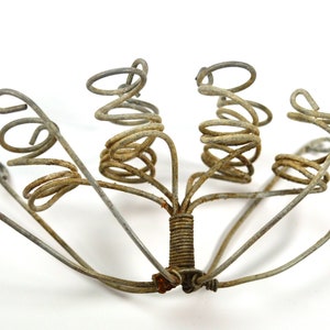Puede incluir: Una escultura de metal hecha de varias piezas de alambre en espiral. La escultura tiene forma de flor con varios tallos y una base central.
