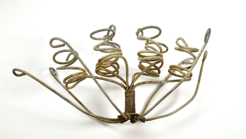 Puede incluir: Una escultura de metal hecha de varias piezas de alambre en espiral. La escultura tiene forma de flor con varios tallos y una base central.
