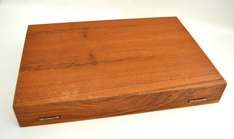 Puede incluir: Una caja de madera con tapa con bisagras y dos bisagras met&aacute;licas. La caja est&aacute; hecha de madera marr&oacute;n claro con un patr&oacute;n de veta natural.