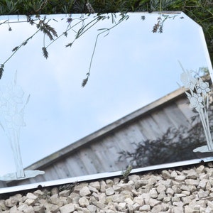 May include: A vintage beveled edge mirror with an etched floral design. The mirror is framed in silver and has a slightly distressed look.