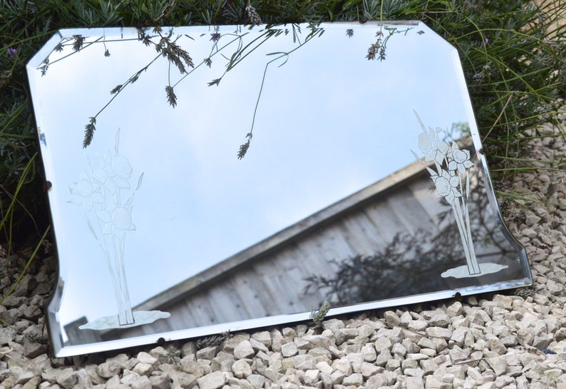 May include: A vintage beveled edge mirror with an etched floral design. The mirror is framed in silver and has a slightly distressed look.