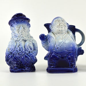Puede incluir: Dos figuras de cerámica de hombres, uno con barba y sombrero, el otro con gafas y estetoscopio, ambos pintados en tonos azules y blancos.