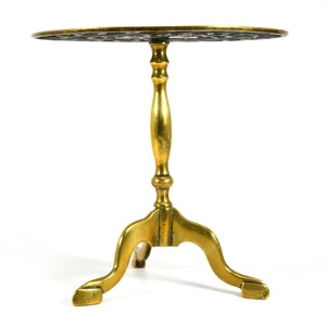 Op de afbeelding: Een kleine, goudkleurige messing tafel met een rond, versierd blad en drie poten. De tafel heeft een eenvoudig, elegant ontwerp.