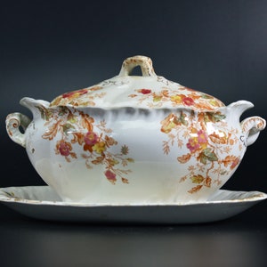 May include: A white porcelain serving dish with a lid, featuring a floral pattern in shades of brown, orange, and pink. The dish has a scalloped edge and two handles.