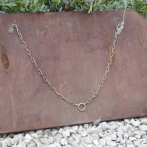 May include: The back of a wooden framed mirror with a metal chain and a ring hanging from it.