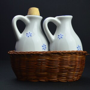 May include: Two white ceramic oil and vinegar bottles with blue floral designs, sitting in a brown wicker basket.