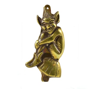 May include: A brass door knocker shaped like a mischievous goblin or imp with a pointed hat and a mischievous grin. The goblin is sitting on a mushroom with its legs crossed.