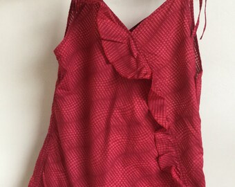 May include: A red camisole top with a dotted pattern and ruffle detail. The top has tie straps and a V-neckline. The fabric appears lightweight. The garment is hanging on a black hanger.