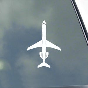 May include: A white airplane decal, featuring a detailed silhouette of a jet. The design includes wings, a tail, and a fuselage with dotted lines. The decal is displayed against a gray background.
