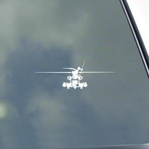 Peut inclure: Autocollant blanc découpé représentant un hélicoptère, avec des éléments de conception détaillés. L'hélicoptère a un rotor principal, un rotor de queue et divers composants. L'autocollant est appliqué sur une fenêtre avec un fond nuageux.