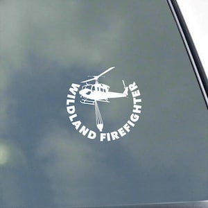 以下が含まれることがあります： ヘリコプターと、そこから落ちるバケツの水を描いた白いビニールステッカー。ヘリコプターの周りに「Wildland Firefighter」という文字が円形に書かれている。