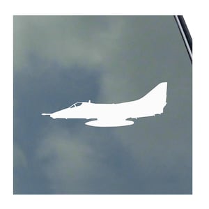 Puede incluir: Una silueta blanca de un avión a reacción, con un fuselaje aerodinámico, una aleta de cola prominente y un diseño de ala distintivo. El avión se representa de perfil, sugiriendo movimiento. El fondo es un cielo nublado borroso.