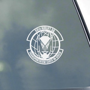 May include: White decal featuring the emblem of the 50th Airlift Squadron. The design includes a stylized face within a globe, surrounded by text that reads "50th Airlift SQ" and "TRANSPORTATEM CERTE IN CAELO".