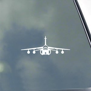 May include: White die-cut decal of a jet aircraft, featuring a central fuselage, wings with multiple pods, and a vertical stabilizer. The design is a simple, clean silhouette, suitable for application on various surfaces.