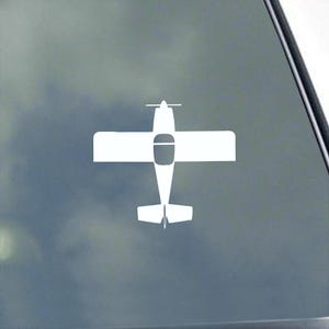 May include: A white airplane decal, featuring a top-down view of a small aircraft. The design includes wings, a fuselage, and a tail, all in a simple, clean style. The decal is likely for a car or window.