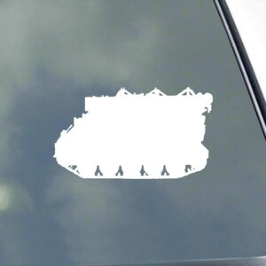 May include: White die-cut vinyl decal of a military tank. The tank silhouette features detailed tracks, a rectangular body, and various top-mounted structures. The decal is designed for application on a vehicle window or similar surface.