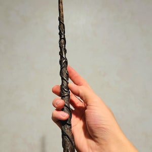 Könnte beinhalten: Ein dunkelbrauner Holzstab mit schwarzen, rankenartigen Details, die um ihn herum gewickelt sind.